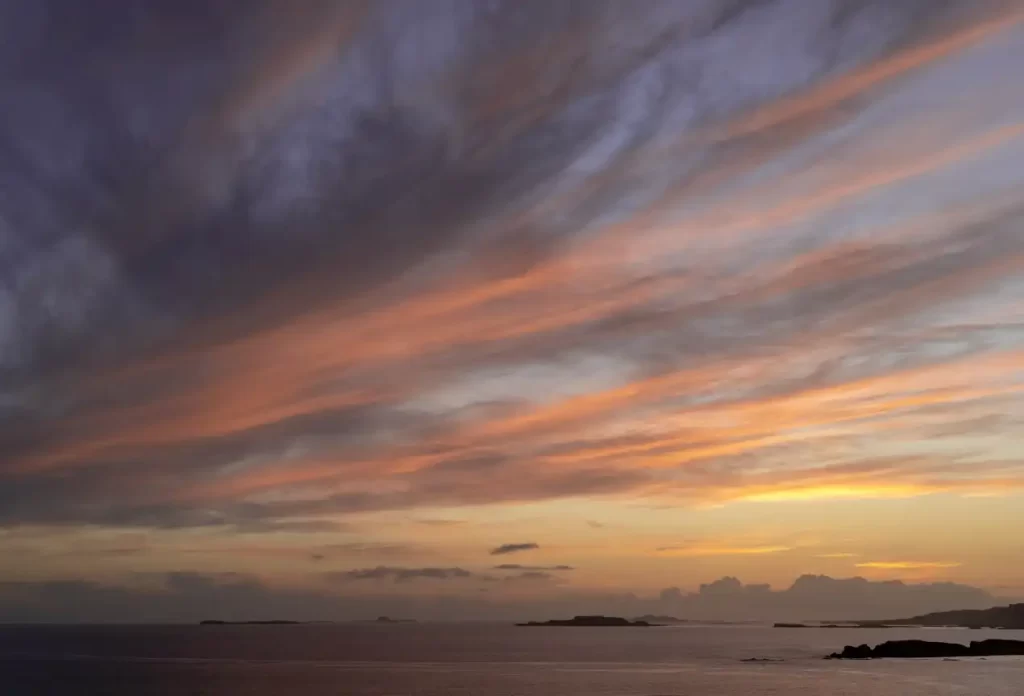A landscape photo showcasing the clouds at sunset on the isle of Mull in Scotland. In the background you can see some rocks protruding out from the loch.