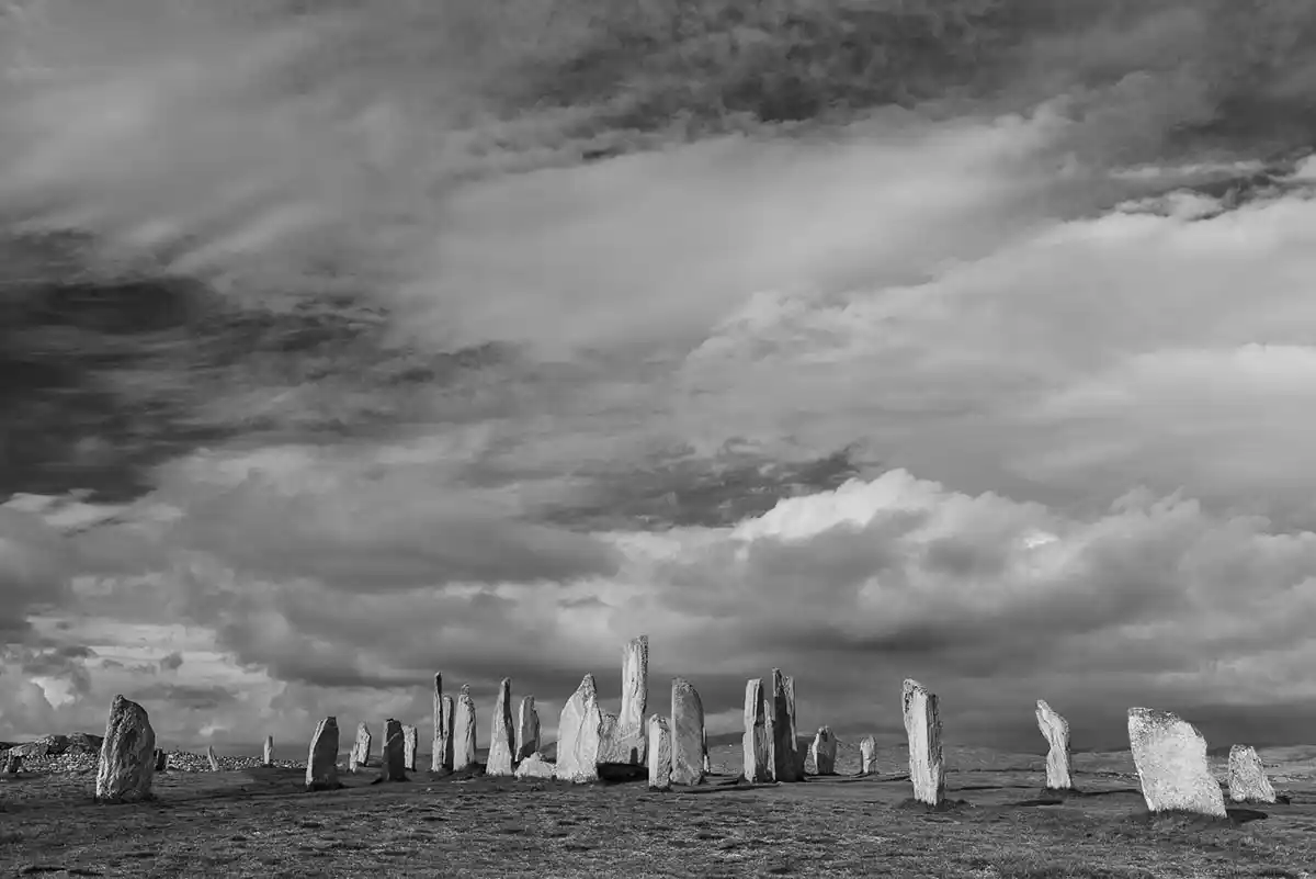 Wide black-and-white view of the Callanish Standing Stones beneath a dramatic cloud-filled sky on the Isle of Lewis.