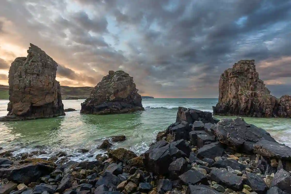 Rocky sea stacks rising from turquoise water beneath a dramatic evening sky at Garry Beach, Isle of Lewis.